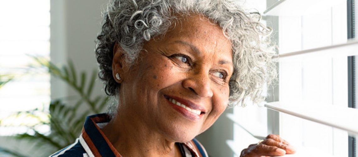 Portrait of smiling african american senior woman looking through window. healthy retirement lifestyle at home.